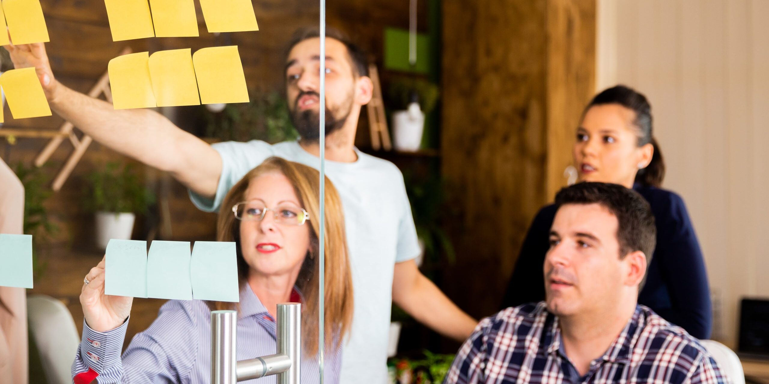 Group of young entrepreneurs looking at sticky notes on a glass window in modern office